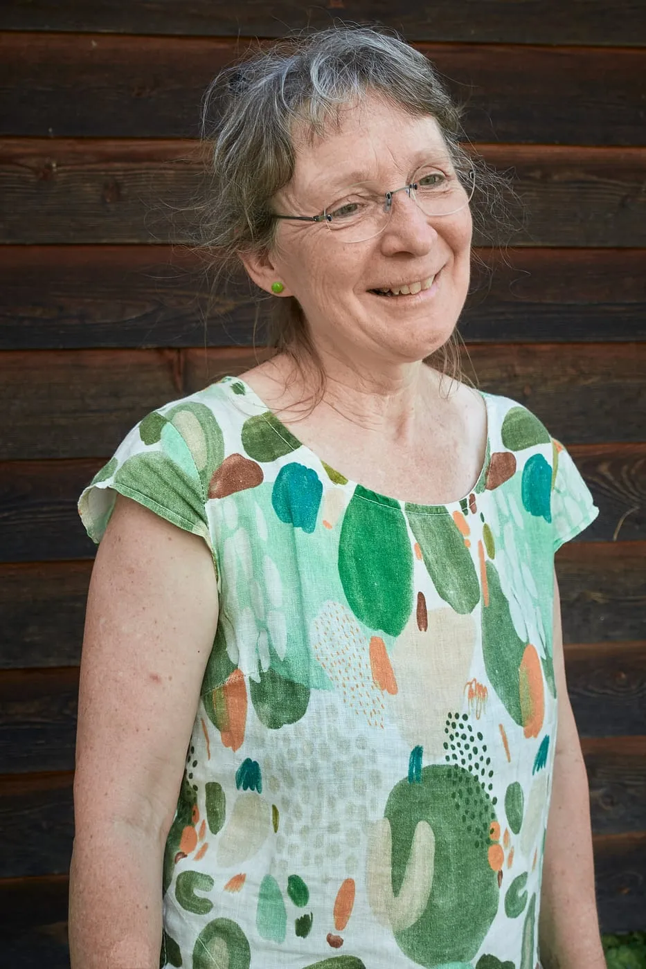Monika Sennhauser vor dunkler Holzfassade, den Kopf zur Seite gedreht und lachend.
